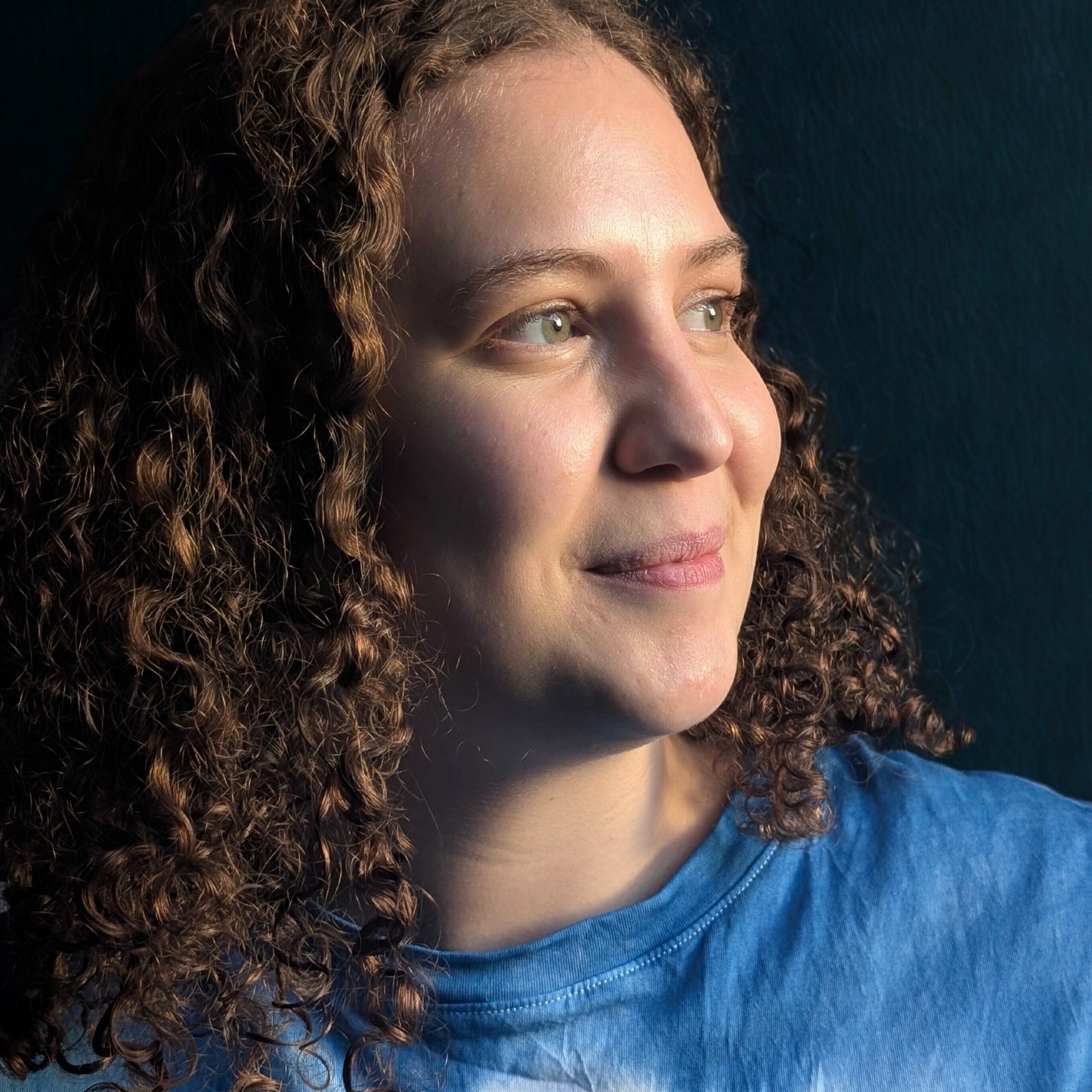 Catherine Doubell in warm side light, with curly brown hair and a blue top, looking away from the camera
