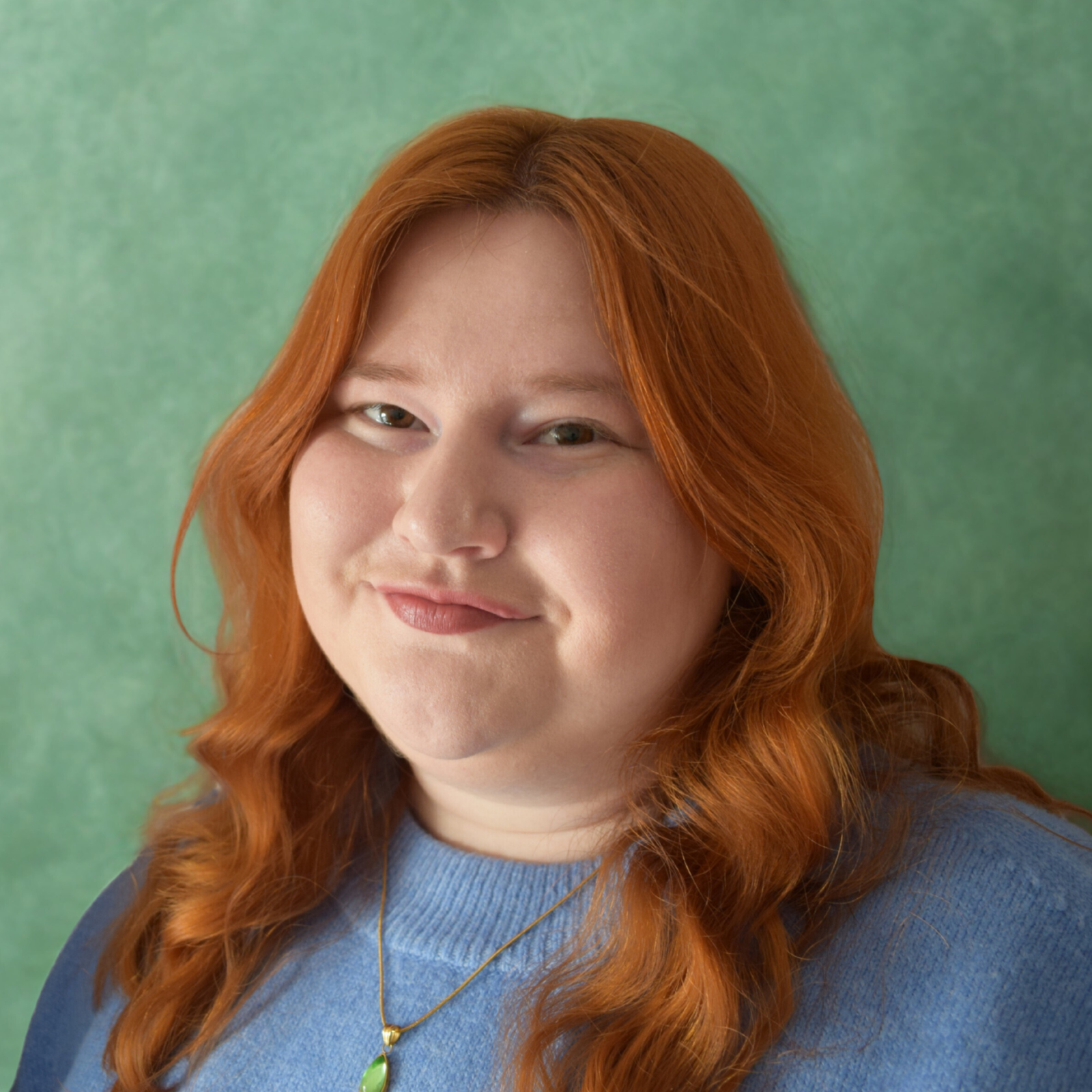 Kate Asquith, smiling, with long red wavy hair and a blue jumper